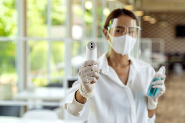 woman with face shield holding thermometer