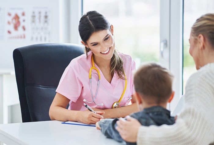 smiling nurse in pink scrubs with young patient