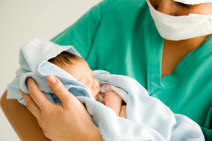 nurse with mask holding newborn baby