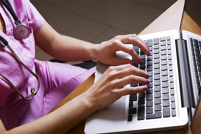 nurse in scrubs reading nursing blogs on laptop