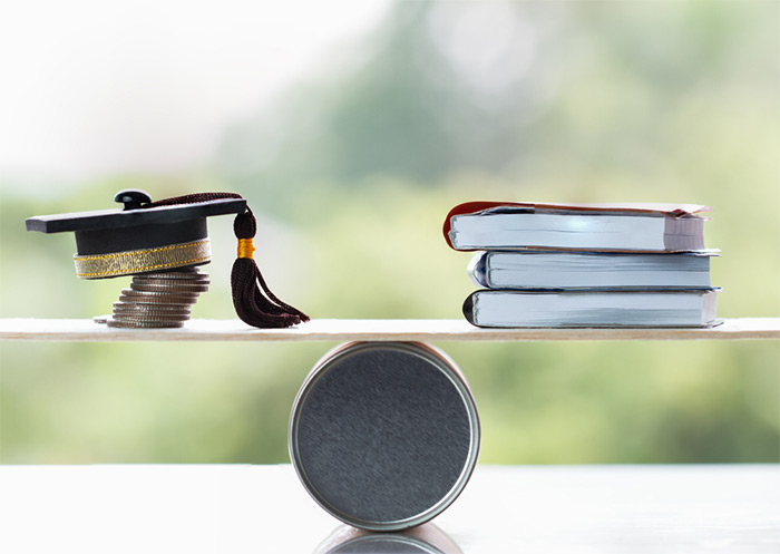 graduation cap on stacked coins and books on balance